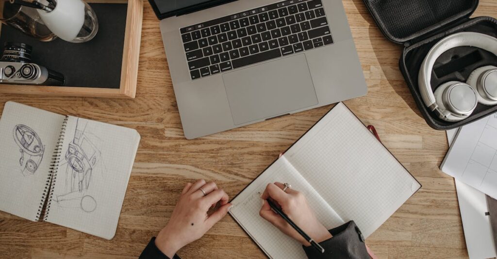 Top view of a creative workspace featuring a laptop, sketchbooks, and headphones on a wooden desk.